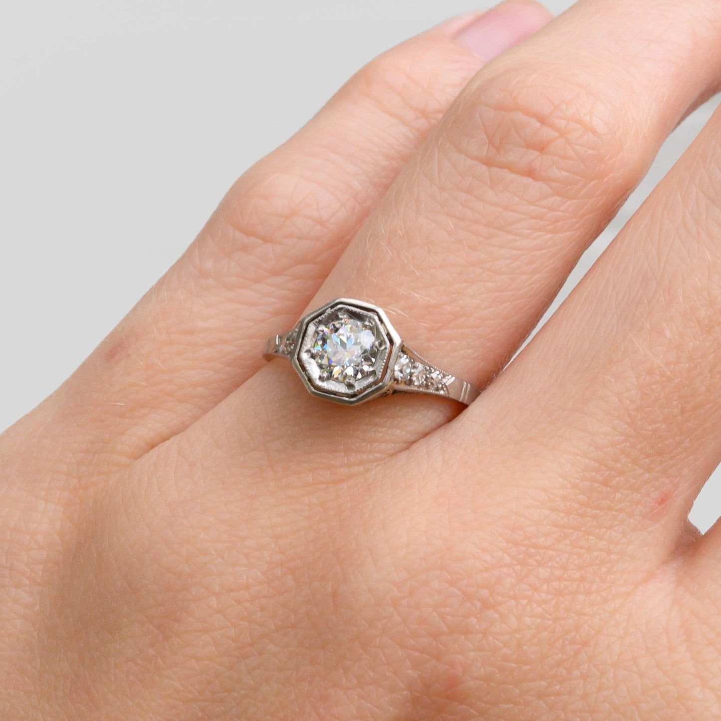 May include: A silver ring with a round, clear diamond in a hexagonal setting. The diamond is surrounded by smaller diamonds.
