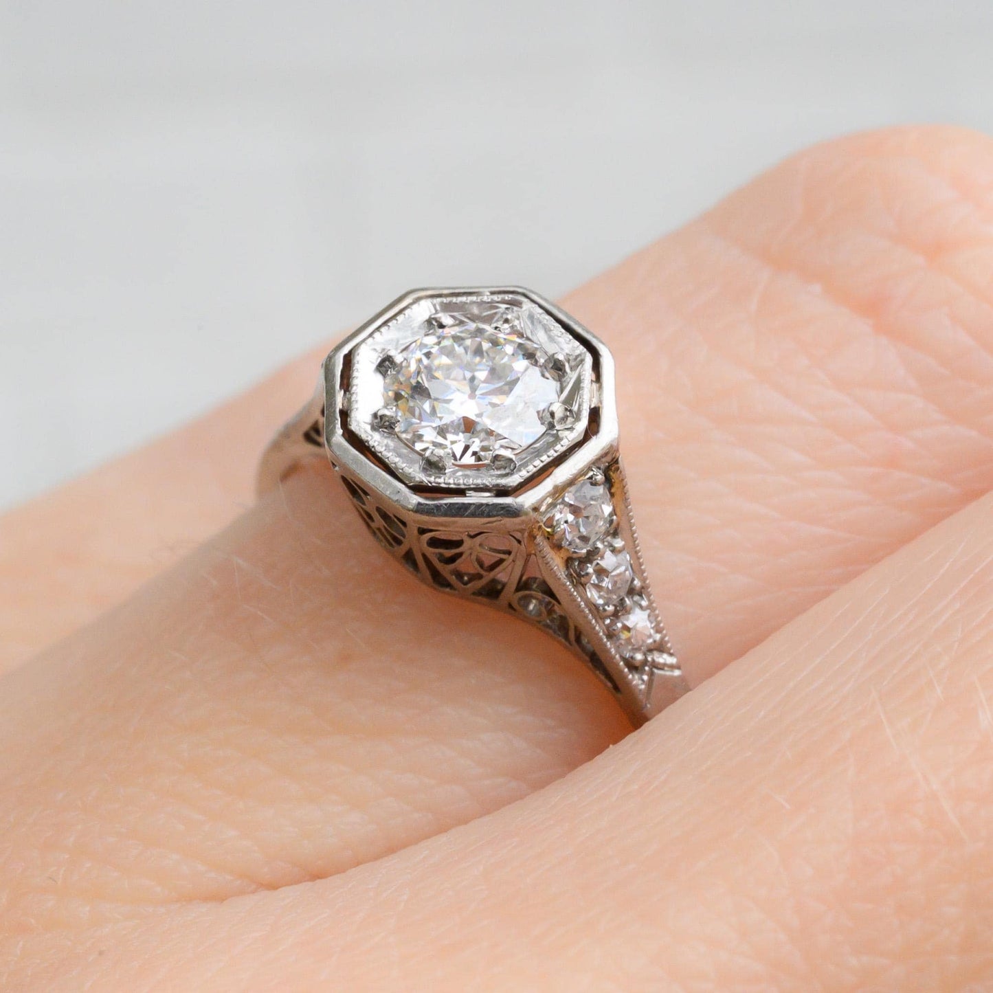 May include: A silver engagement ring with a large octagon-shaped diamond center stone surrounded by smaller diamonds. The ring has a filigree design and is set on a silver band.
