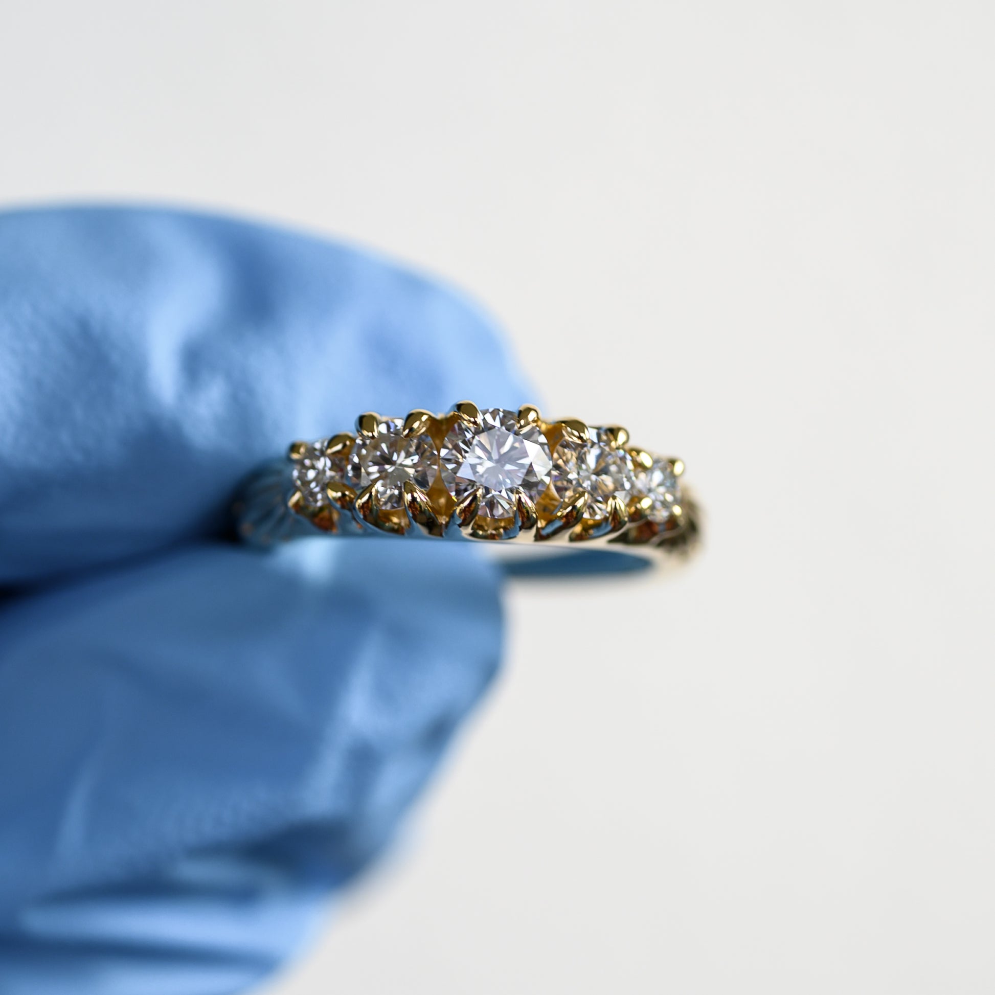 Gold ring with diamonds held by a gloved hand on a light background