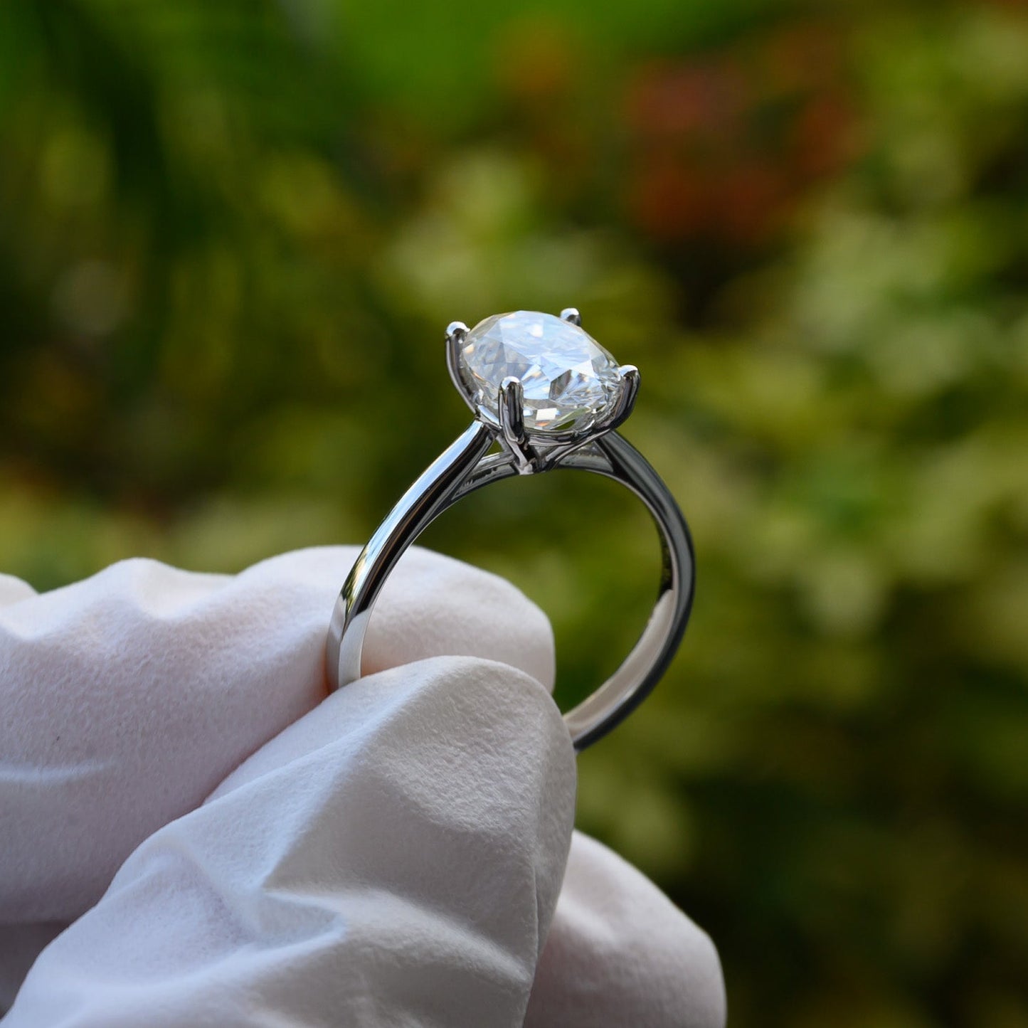 Diamond ring held by a gloved hand with a blurred green outdoor background