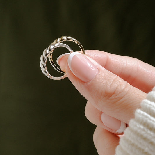 May include: Two gold rings, one with a twisted design and the other with a smooth band, are stacked together.